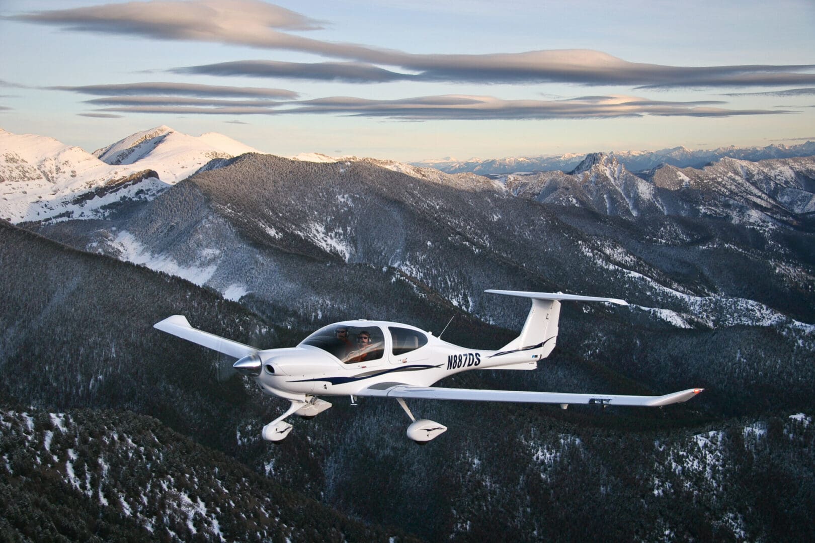 A small white plane flying over the mountains.