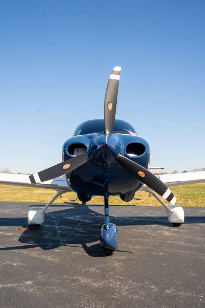 A sleek blue propeller airplane parked on the runway under a clear blue sky.
